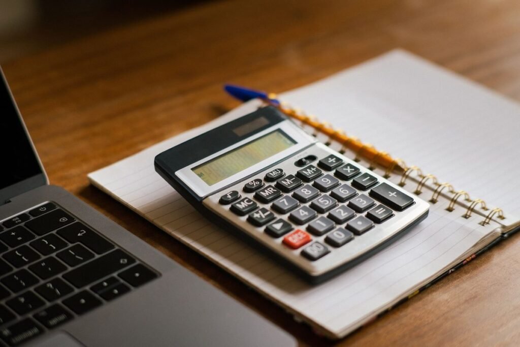 Calculadora y cuaderno abierto junto a una laptop sobre un escritorio de madera