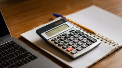 Calculadora y cuaderno abierto junto a una laptop sobre un escritorio de madera