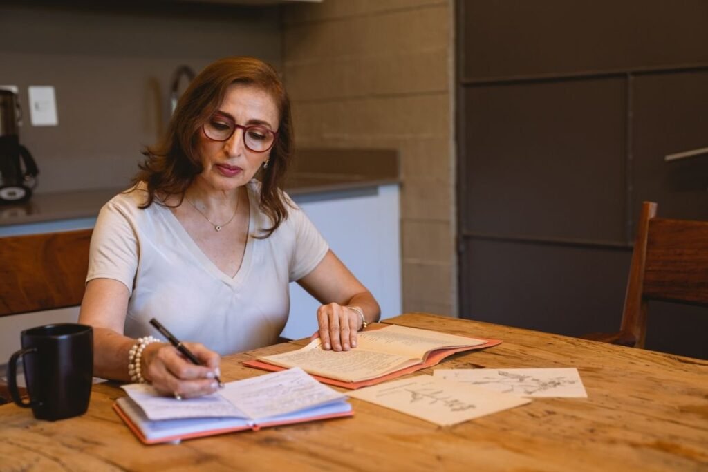 Mujer escribe notas en un cuaderno sobre una mesa de madera en casa
