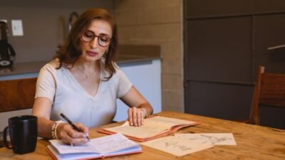 Mujer escribe notas en un cuaderno sobre una mesa de madera en casa