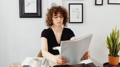 Mujer con lentes revisa documentos sentada frente a su escritorio